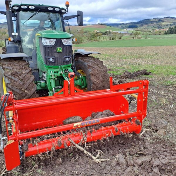 godet ramasse pierre de face, en plein travail dans la terre, attelé à l'avant d'un tracteur