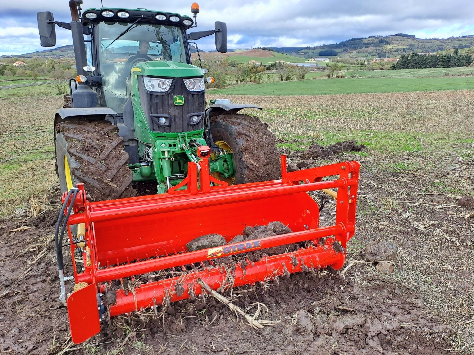 godet ramasse pierre de face, en plein travail dans la terre, attelé à l'avant d'un tracteur