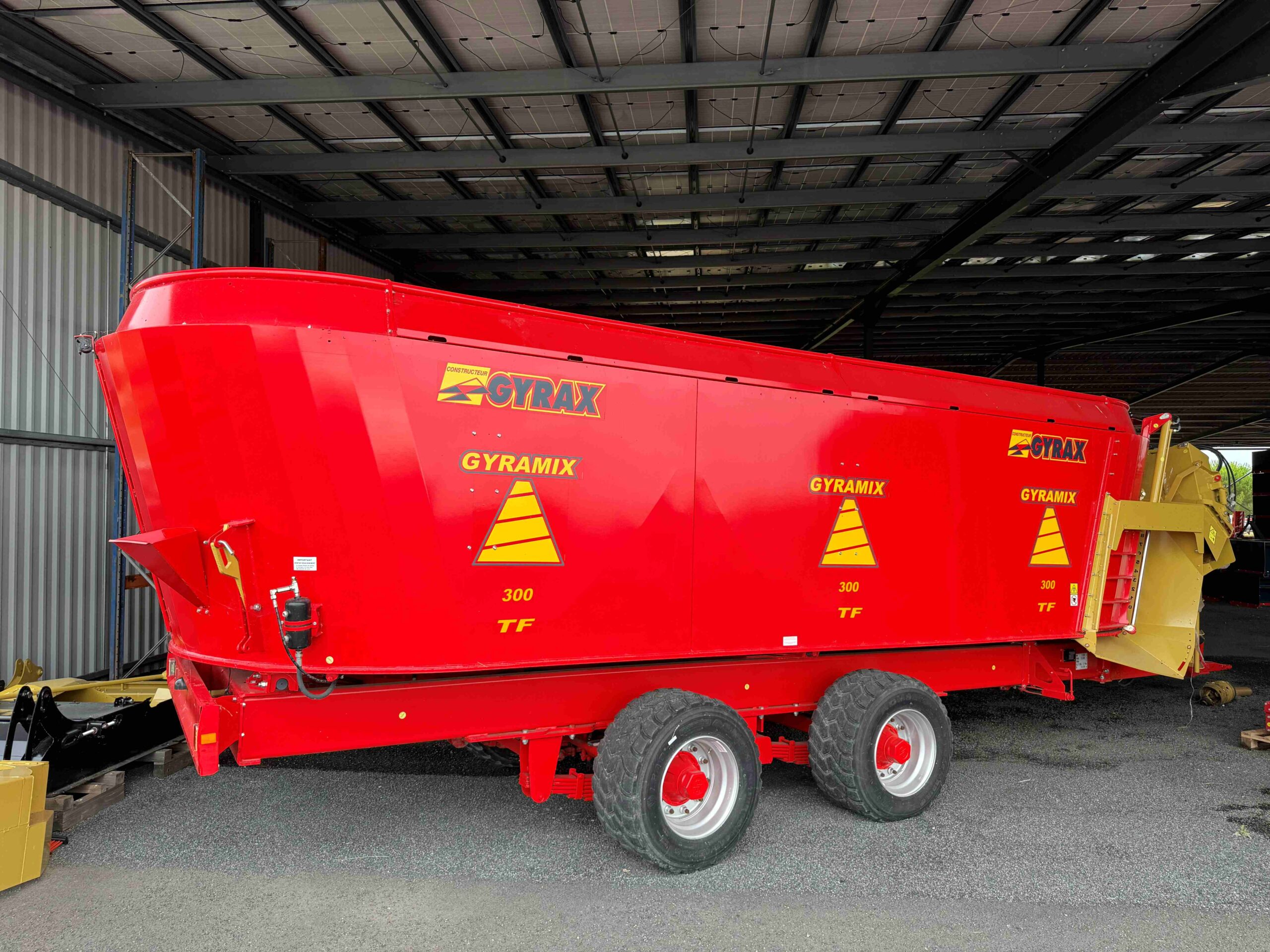 Mélangeuse trivis rouge de marque Gyrax, entreposé sous un hangar et vue de profil