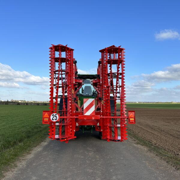 Vu arrière d'un cultivateur 3 poutres replié Gyrax. Attelé à l'arrière d'un tracteur sur une petite route.