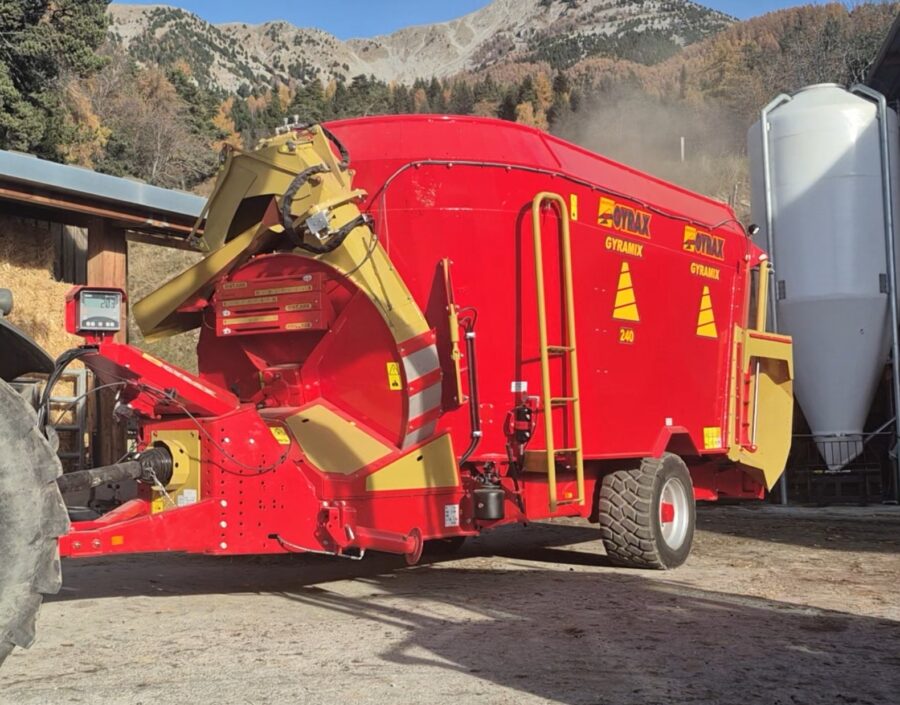 Mélangeuse rouge double vis de marque Gyrax, attelée derrière un tracteur, prêt à distribuer.