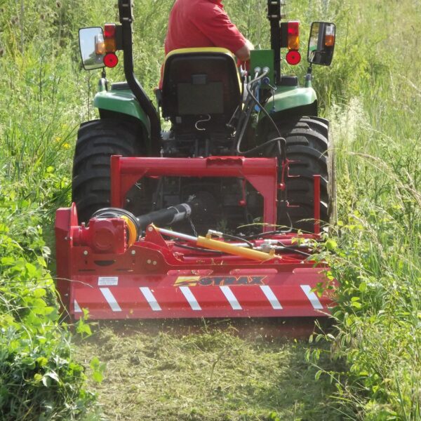 Roto-faucheuse rouge Gyrax, modèle RFL (loisir), vue 3/4 arrière attelée sur un micro tracteur, coupant des herbes tres hautes dans un champs. position repliée à l'arrière du tracteur en horizontal