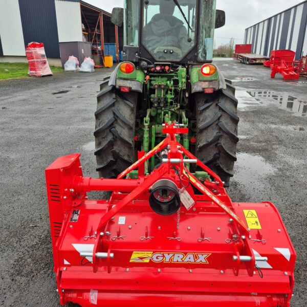 Broyeur horizontal vignes et vergers rouge Gyrax, vue arrière attelé à un tracteur, sur parking.