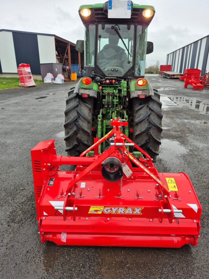 Broyeur horizontal vignes et vergers rouge Gyrax, vue arrière attelé à un tracteur, sur parking.