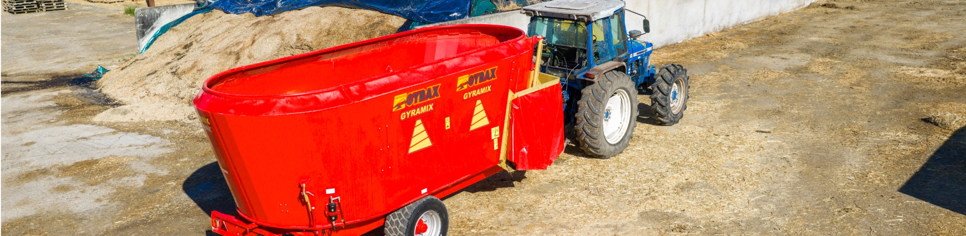 Mélangeuse de marque Gyrax, attelée derrière un tracteur dans une cour de ferme.