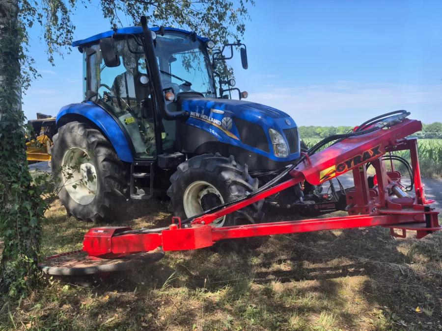 Broyeur sous cloture Gyrax attelé à l'avant d'un tracteur, en action contre un pied d'arbre.